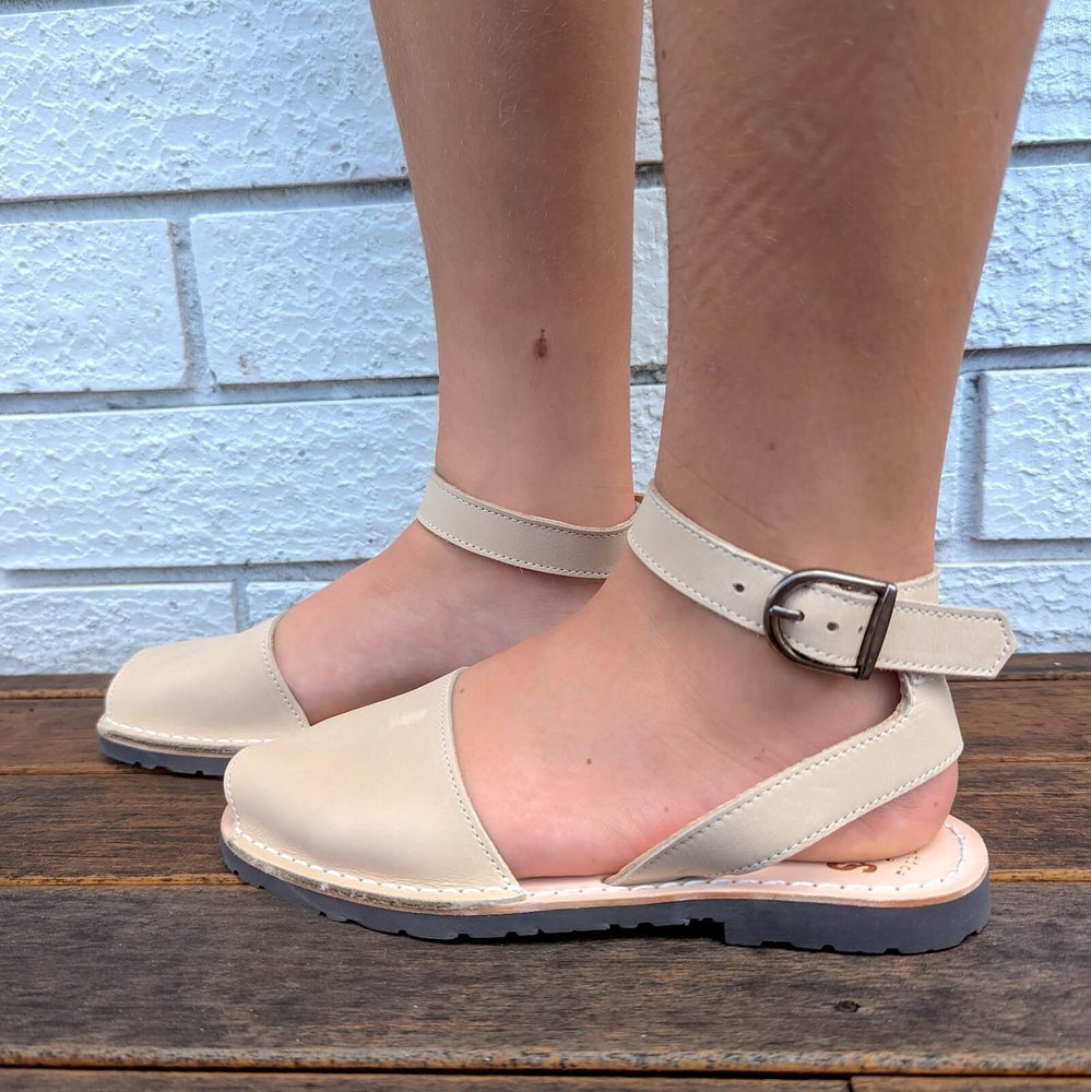 Young lady wearing ankle sandals in leather beige, standing.